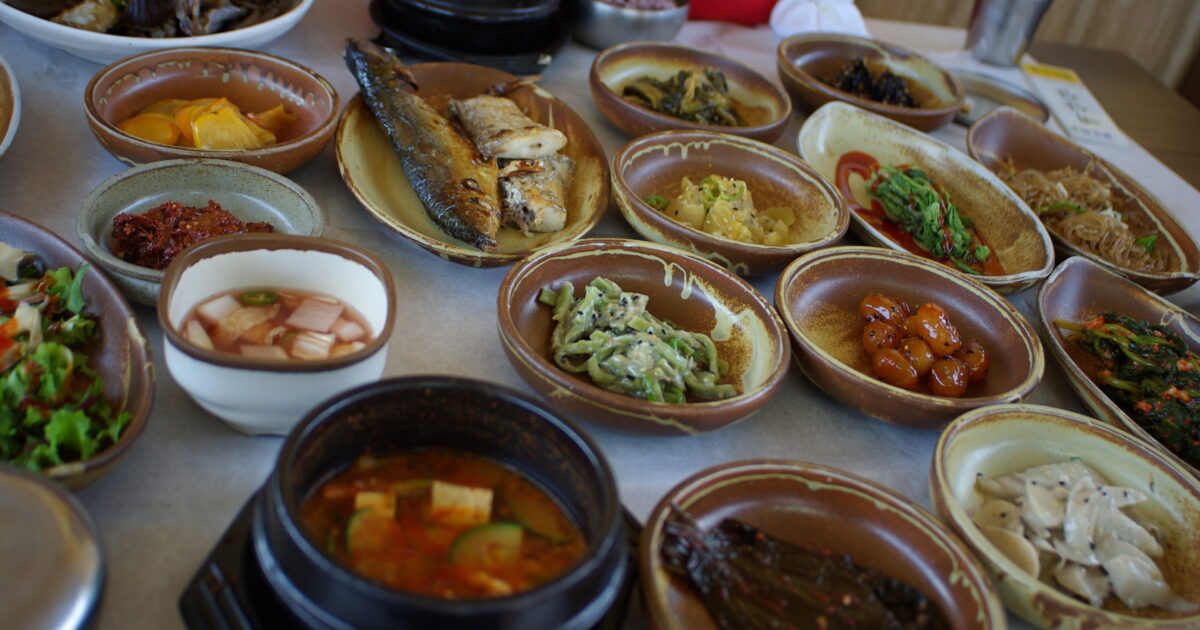 Mesa repleta de banchan y platos coreanos, como en un mukbang